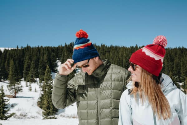 Man and woman wearing custom made beanies in the mountains